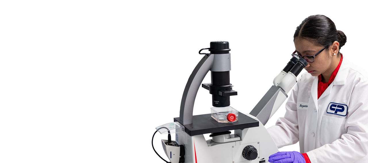 Cientista de bata branca e luvas roxas a utilizar um microscópio de laboratório avançado sobre um fundo preto.