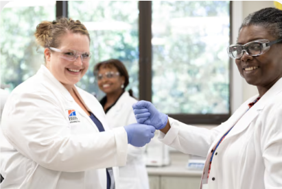 Dois cientistas com batas de laboratório e luvas sorriem e apertam as mãos num ambiente de laboratório.