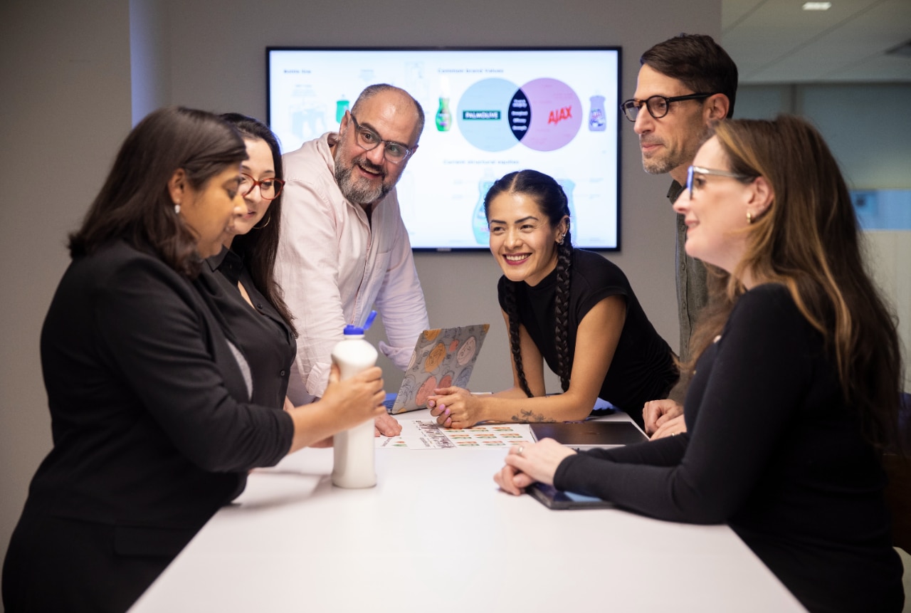 A team working together. In the background, an interactive board with the Palmolive and Ajax logos